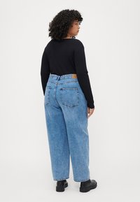 Hoge taille blauwe denim jeans met een ontspannen pasvorm, vijf zakken en een tan leren label op de achterkant. Gepaard met een zwart langhemd.