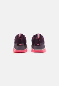 Schwarze und rosa Sportschuhe mit einem Mesh-Obermaterial, auffälliger Markenkennung und einem gepolsterten Kragen. Die Sohle hat einen soliden rosa Akzent.
