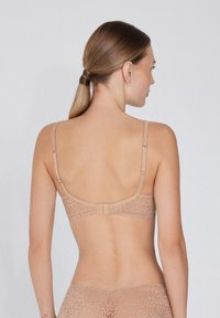 Sostén de encaje en color nude con tirantes ajustables, cierre de gancho y ojal, y patrón floral. Textura suave y diseño minimalista.