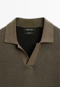 Bomulds-polo-sweater i olivengrøn med et tekstureret, vaffelmønster, V-hals og en kontrastfarvet krave. Brandlabel synlig.