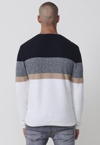 Sudadera de manga larga con un diseño texturizado que presenta rayas horizontales en navy, gris, beige y blanco. Textura de tejido acanalado en toda la prenda.