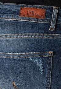 Farkkuhousut tummansinisellä pesulla, joissa on nahkainen etiketti, jossa lukee "LTB", näkyvät saumat, kuluneet tahrat ja klassinen taskusuunnittelu.