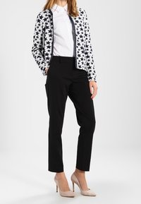 Marineblauwe en witte blazer met sterrenpatroon over een wit overhemd, gecombineerd met zwarte broek en beige hoge hakken. Soepele stof en getailleerde pasvorm.