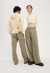 Beige hooded sweatshirt, ribbed white cropped top, and olive baggy sweatpants worn with black chunky platform shoes.