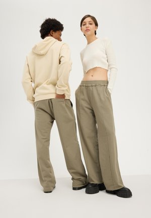 Sweatshirt beige à capuche, top court blanc côtelé, et pantalon de survêtement ample olive porté avec des chaussures compensées noires.
