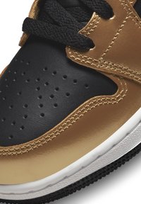 Tenisky s černým koženým svrškem a zlatými akcenty. Texturovaný povrch, perforace a černé tkaničky. Bílá mezipodešev s gumovou podešví.