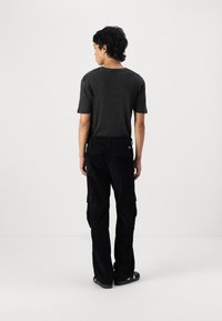Sort kortærmet t-shirt med ribbet tekstur, parret med sorte cargo-bukser med sidelommer og en afslappet pasform, set fra ryggen.
