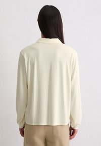 Lichtgele lange mouw shirt met een kraag, gladde stof en een ontspannen pasvorm. Draag het met beige broek, met zicht op de achterkant.