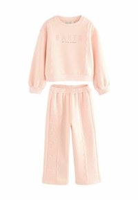 Ensemble de jogging rose clair comprenant un sweat cropped avec des détails en dentelle et un pantalon à jambes larges assorti avec une taille élastique.