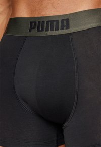 Črne bokserice z zelenim elastičnim pasom s pisanjem "PUMA". Tkanina je gladka z ravnimi šivi za udobje.
