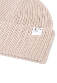 Berretto beige lavorato a maglia con texture a coste e risvolto. Presenta un'etichetta bianca con testo nero su un lato. Materiale morbido in misto lana.