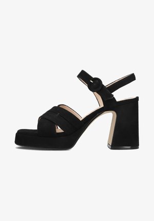 Zwart suède hoge hak sandaal met brede band over de tenen, gespdetail bij de enkel en stevige blokhak. Soepele textuur en strakke lijnen.