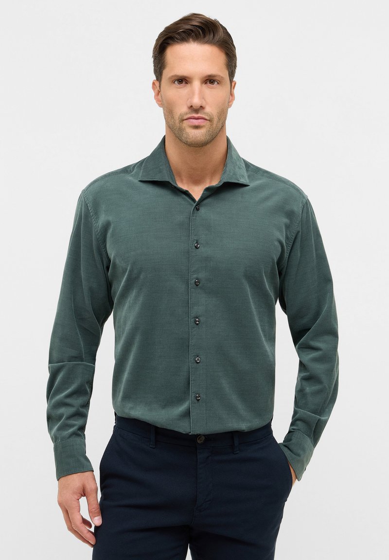 Camicia a maniche lunghe di colore verde scuro, realizzata in tessuto texturizzato. Presenta un colletto a punta, sei bottoni neri lungo la parte anteriore e polsini aderenti.