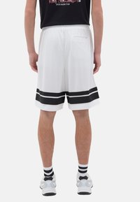 Shorts deportivos blancos con rayas negras en el dobladillo, hechos de material de malla, que cuentan con un bolsillo trasero y una banda elástica en la cintura.