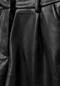 Svart läderkjol med en slät yta, bälte i midjan och sidofickor, vilket framhäver ett mjukt, premium material.