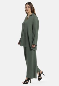 Grøn to-delt sæt lavet af struktureret stof. Skjorten har et knaplukningsdesign med krave, og bukserne er løstsiddende.