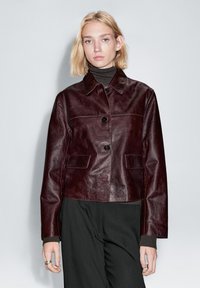 Bourgogne læderjakke med krave, lukning med knapper foran og to sidelommer. Glat tekstur med en let skinnende finish.