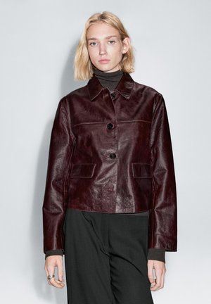 Bordeauxrode leren jas met een kraag, knoopsluiting aan de voorkant en twee zijzakken. Glad materiaal met een licht glanzende afwerking.