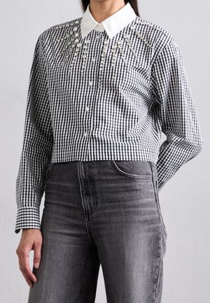 Mujer con una camisa cropped de cuadros blancos y negros con cuello blanco y pedrería decorativa, combinada con vaqueros de tiro alto de color gris oscuro.