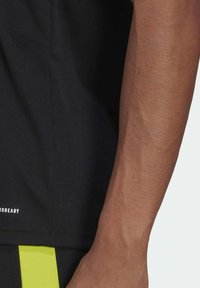 Black athletic shirt made of smooth fabric, with short sleeves and a straight cut. Features reflective accents and a logo at the hem.