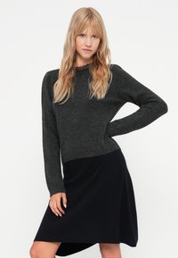 Mørk grå strikket genser med lange ermer, med en blonde halslinning, sammen med et mørkeblått skjørt med asymmetrisk linning. Myk tekstur og avslappet passform.