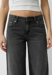 Široké tmavě šedé džíny z denimu. Mají zapínání na knoflík a zip, pět kapes a jemné vyblednutí látky.