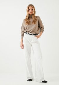 Beige kaulusneule, löysä malli; valkoiset leveälahkeiset farkut; musta vyö; mustat neliönmalliset kengät. Minimalistinen muotoilu neutraalilla värimaailmalla.