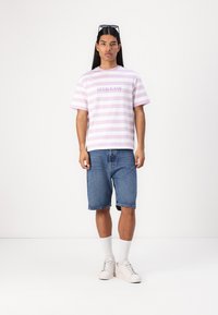 Strikket t-skjorte med korte ermer i lys rosa og hvit med "GUESS JEANS"-logo. Brukt med denimshorts og hvite joggesko, med hvite sokker.