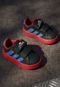 Black sneakers with red soles and accents, featuring blue web patterns and dual Velcro straps. Includes a "Spider-Man" logo.