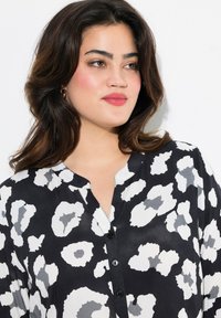 Schwarze Bluse mit einem Leopardenmuster in Weiß und Grau, mit einer Knopfleiste und einem kragenlosen Design. Glattes, leichtes Material.