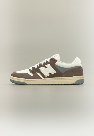 Zapatilla New Balance marrón y blanca con detalles en gris y cordones blancos, mostrada de perfil sobre un fondo neutro.