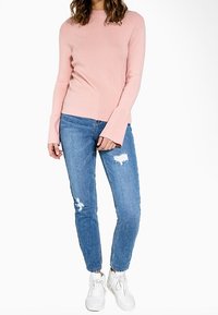 Pull long à manches longues rose clair avec un col rond, associé à un jean bleu déchiré et des baskets blanches, avec une coupe ajustée.
