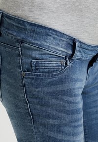 Blå denimjeans med slim fit och blekta områden. Har två framfickor med dekorativ sömnad och metallnit.