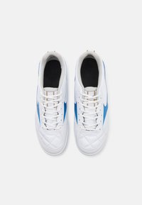 Scarpe da ginnastica bianche con superficie a trama diamantata, dettagli laterali blu e lacci bianchi. Fodera interna nera e dettagli dorati sulla linguetta.