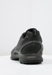 Scarpa sportiva nera con parte superiore testurizzata, colletto imbottito e suola in gomma chunky con un design del tallone liscio.
