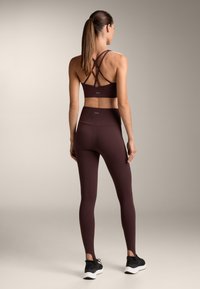 Sutien sport de culoare vișinie cu bretele încrucișate, asortat cu colanți înalți pe talie. Textură netedă, design elegant și pantofi sport negri.