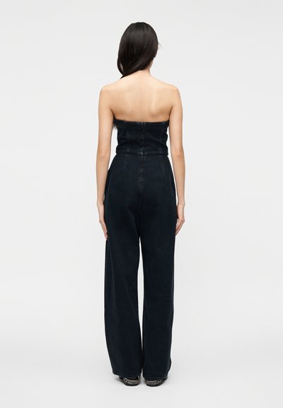 Rihmadeta mustast teksariidest kombinesoon laia säärega, õmblusteta seljaosaga ning istuva ülakehaga. Valmistatud vastupidavast kangast, minimalistlike disainielementidega.