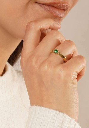 Gold ring with a round green gemstone, featuring a smooth band and a subtle interplay of light on its polished surface.