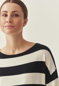 Pull rayé marine et crème avec un large col, texture douce et coupe décontractée. Rayures horizontales sur un tissu léger.