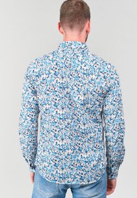 Una camicia floreale con un motivo blu e bianco, realizzata in tessuto leggero, con colletto classico e polsini con bottoni.