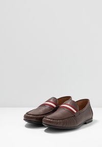Mocassins en cuir marron à finition texturée, avec des rayures horizontales rouges et blanches sur le cou-de-pied. Style à enfiler avec une semelle flexible.