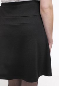 Mustat, liehuvat hameet, joissa on sileä pinta ja muotoiltu vyötärö. Sisältää polvenpituuden ja yksinkertaisen, minimalistisen muotoilun.