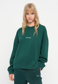 Felpa in cotone verde con vestibilità rilassata, polsini e orlo a costine, con il logo bianco "PEGAADOR" sul petto.