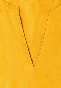 Tissu jaune vif avec un col en V profond et des détails de coutures visibles autour de l'encolure.