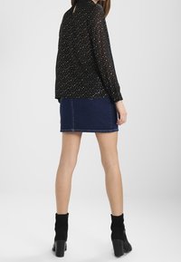 Blusa nera a maniche lunghe con colletto e speckles dorati, abbinata a una mini gonna di denim scuro. Stivali neri alla caviglia completano il look.