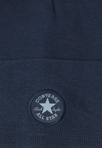 Căciulă tricotată bleumarin cu un patch circular Converse All Star, având un emblemă cu stea și textul "Chuck Taylor".