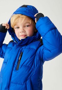 Zila pūkainā jaka ar augstu apkakli, ar rāvējslēdzēja kabatu un melniem akcentiem uz pleciem. Iedvesmojusi izšūta tekstūra un noņemama kapuce.