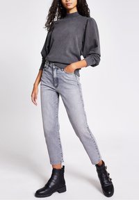 Grauer Sweatshirt mit hohem Kragen und Puffärmeln, kombiniert mit hoch taillierten, hellgrauen Jeans. Schwarze Knöchelstiefel mit Riemenakzenten.