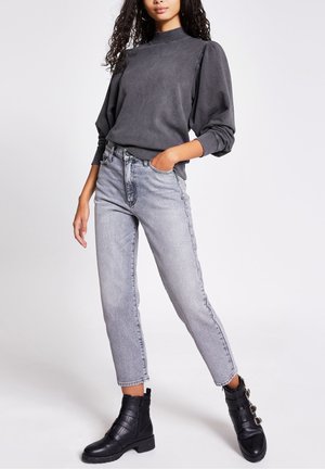 Grauer Sweatshirt mit hohem Kragen und Puffärmeln, kombiniert mit hoch taillierten, hellgrauen Jeans. Schwarze Knöchelstiefel mit Riemenakzenten.