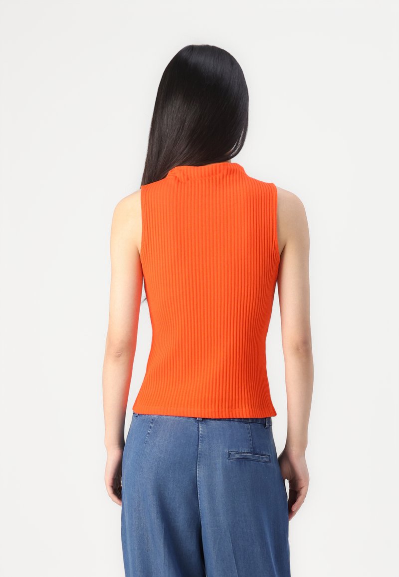 Haut orange côtelé sans manches avec un col montant et une coupe ajustée, associé à un pantalon en denim avec des détails de poche arrière.